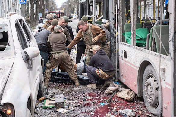 Os militares ucranianos carregam um corpo morto de um trolleybus após uma greve de mísseis russos em Sumy no domingo de Palm.