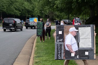 Activists hold signs as the motorcade for President Donald Trump departs Trump National Golf Club on May 24.