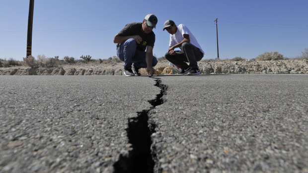A crack caused by an earthquake on highway 178 outside of Ridgecrest, California is examined by Ron Mikulaco, left, and his nephew, Brad Fernandez.