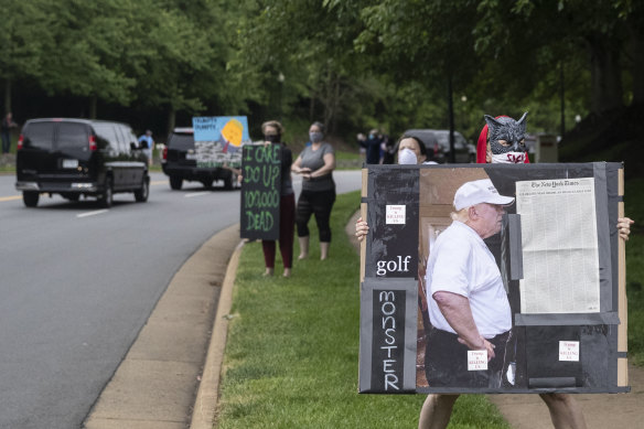 Activists hold signs as the motorcade for President Donald Trump departs Trump National Golf Club on May 24.