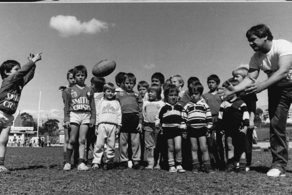 Rabbitohs Coach George Piggins passes the ball to 4 year old Braith Anastasakis of Malabar at Redfern Oval in 1986.
