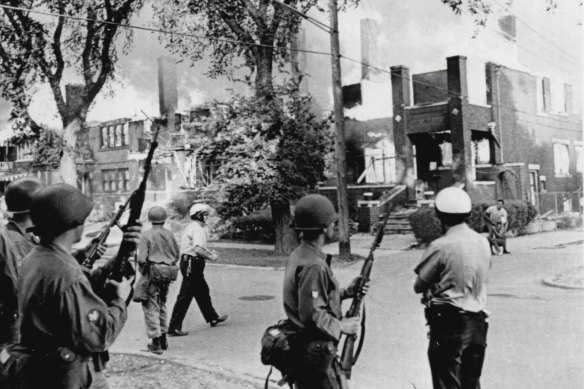 Police and National Guardsmen stand by as fire sweeps through a city block in the wake of race riots in Detroit in 1967.