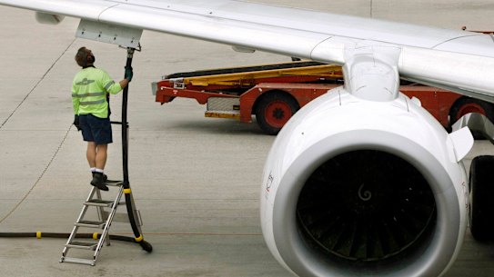 A ground staff member stands beside a fuel attachment to a Qantas plane at Sydney Airport.