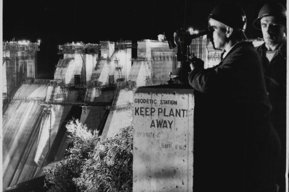 Silhouetted against the floodlit wall of Warragamba Dam, a surveyor sights his theodolite to check any movement of the wall in February 1960.
