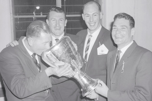 Melbourne coach Norm Smith drinks a victory toast from the 1960 VFL premiership cup, watched by John Beckwith, John Lord and Barassi after their win over Collingwood.