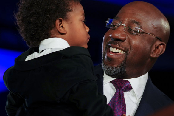 Democratic Senator Raphael Warnock holds his son Caleb Warnock during an election night watch party in Atlanta. Warnock, a pastor, beat Trump-backed Republican challenger Herschel Walker in a run-off election in Georgia.