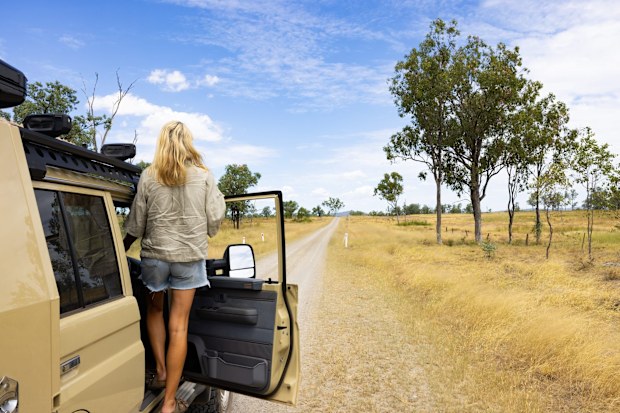 A woman stands on the side of her car looking at an empty Outback road