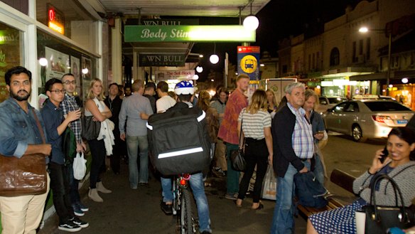 A food delivery cyclist on King Street in Newtown rides on the footpath through a busy bus stop.