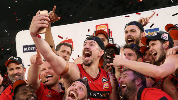 Wild times: Perth's Greg Hire takes a team selfie with the trophy after claiming the NBL championship on Sunday.