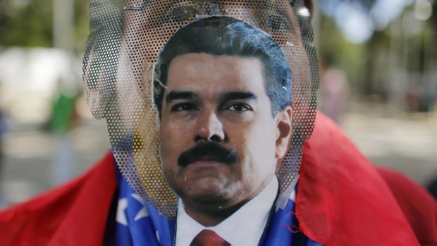 A pro-government protester wears a make-shift mask with an image of President Nicolas Maduro taped to it in Caracas.