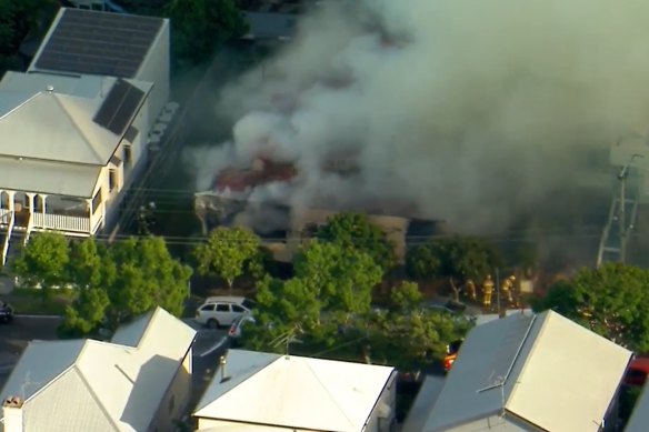 A Dutton Park house burns on Tuesday afternoon, with fire crews visible to the right.
