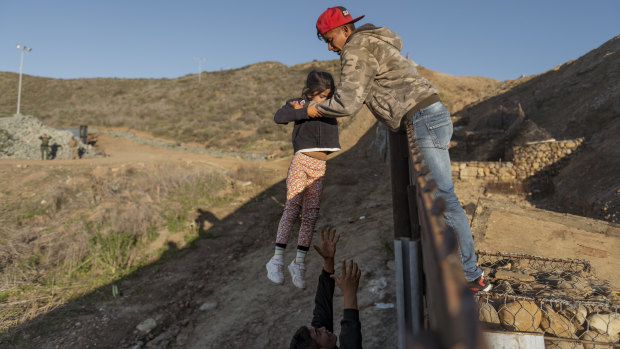 A migrant from Honduras pass a child to her father after he jumped the border fence to get into the US side to San Diego, California, from Tijuana, Mexico. 