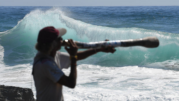 Local Russell Corowa playing the didgeridoo at Snapper Rocks on the Gold Coast, while huge swells and high tides are set to pummel south-east Queensland beaches over the coming days.