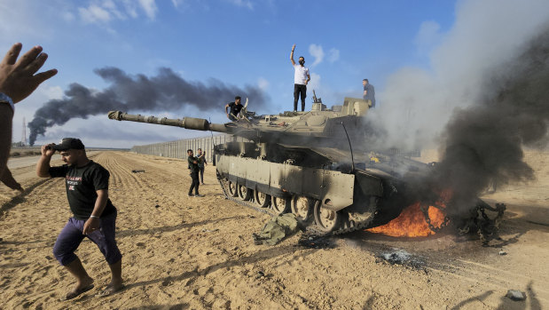 Palestinians celebrate by a destroyed Israeli tank at the Gaza Strip fence.