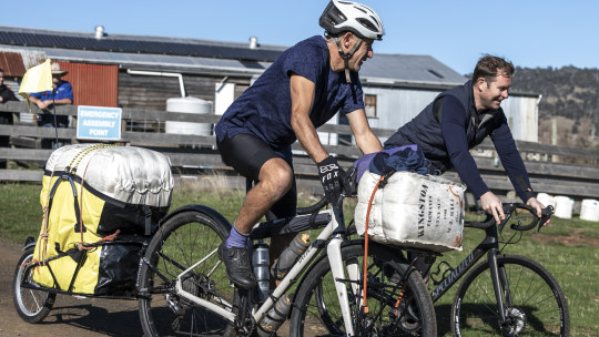 Sailor/adventurer Grant Maddock (white helmet) and M.J. Bale CEO and founder Matt Jensen riding bikes to Hobart with wool bales - as they aim to produce possibly the world’s first net zero-emission woollen knitwear.