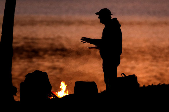 FILE IMAGE: A man warms himself next to a campfire at dusk.