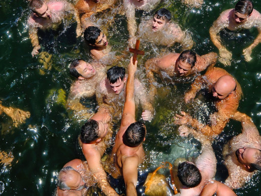 Swimmers crowd around Steve Kikyris, holding the cross, at the end of the race.