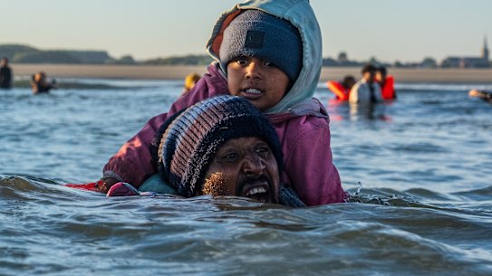 GRAVELINES, FRANÇA - 25 DE AGOSTO: Um homem luta em águas profundas enquanto carrega uma criança nos ombros para tentar embarcar em um bote migrante no Canal da Mancha em 25 de agosto de 2025 em Gravelines, França. As travessias de migrantes por barco causaram muita controvérsia no Reino Unido, com grupos de extrema direita organizando manifestações em frente aos hotéis que abrigam migrantes em todo o país durante o verão. No final de Agosto de 2025, mais de 28.000 migrantes cruzaram o Canal da Mancha em pequenos barcos este ano. (Foto de Carl Court/Getty Images)