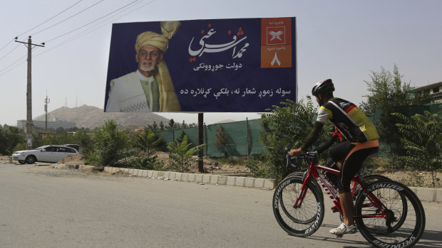 Afghan men cycle past an election poster of presidential candidate Ashraf Ghani in Kabul.