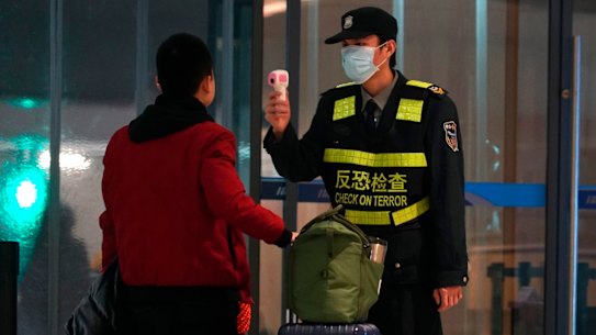 An airport staff member uses a temperature gun to check people leaving Wuhan Tianhe International Airport.
