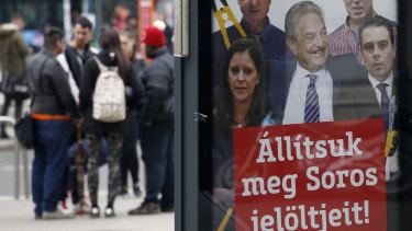People stand on a street by a billboard from Prime Minister Viktor Orban's Fidesz party reads "Let's stop Soros' candidates!" showing American financier George Soros, centre.