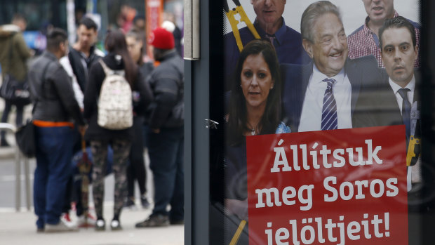 People stand on a street by a billboard from Prime Minister Viktor Orban's Fidesz party reads "Let's stop Soros' candidates!" showing American financier George Soros, centre.