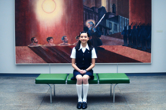 The mysterious Miss Huang (Sarah Bock), in front of a painting of Kier Eagan in wrathful mood.