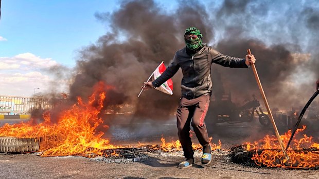 An anti-government protester stands near burning tires set fire to close a street during a demonstration against the newly appointed Prime Minister Mohammed Allawi in Najaf. 