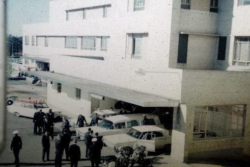 Secret Service agents and police officers look on as the white hearse is opened to load the casket of president John F. Kennedy at Parkland Hospital in Dallas on November 22, 1963.