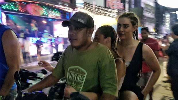 Ignoring safety, two girls ride on a scooter taxi without a helmet in Bali.