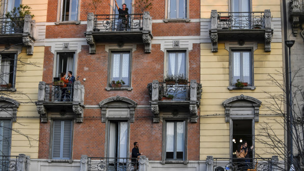People in lockdown stand on their balconies in Milan, Italy.
