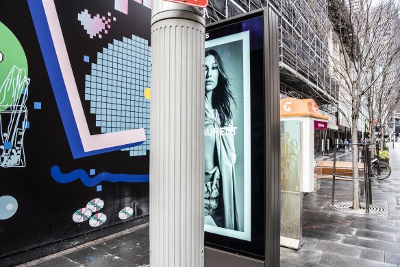 This footpath is crowded with a pole, digital billboard and a phone booth.