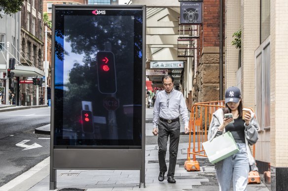 Pedestrians pass a QMS billboard on Liverpool Street in the Sydney CBD.