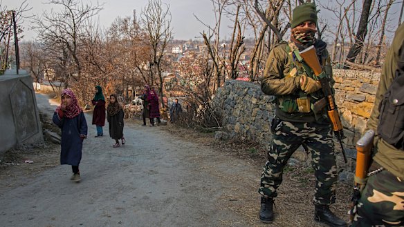 Young children walk past a paramilitary soldier in Kashmir, where India’s security crackdown is a familiar scene.