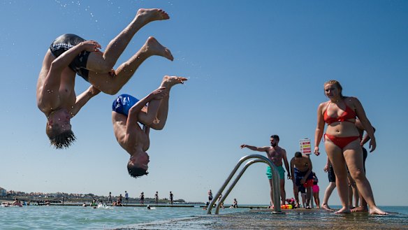 Boys somersault into the water from the lido jetty wall at Margate beach in England.