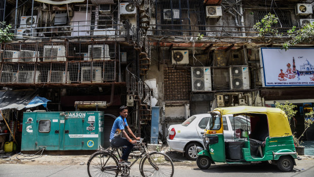 A man cycles past a facade with rows of air conditioners on a hot summer afternoon in New Delhi.