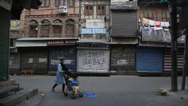 A Kashmiri woman pushes a child on a stroller past a closed market in Srinagar, Indian controlled Kashmir on Tuesday.