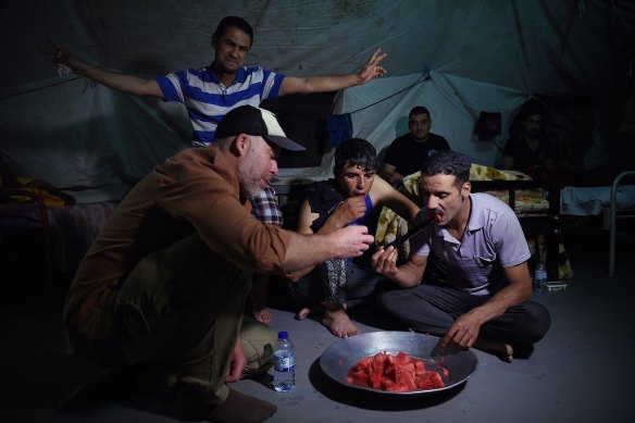 Michael Bachelard, left, eats watermelon off a dagger with Iraq’s Golden Division soldiers in their Mosul barracks on June 29, 2017.