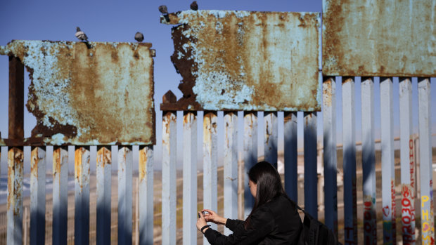 A woman takes pictures as birds sit along a rusted top section of the border wall near Tijuana, Mexico.