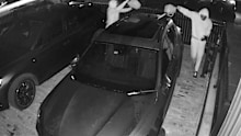 Two masked men pour accelerant on a car.