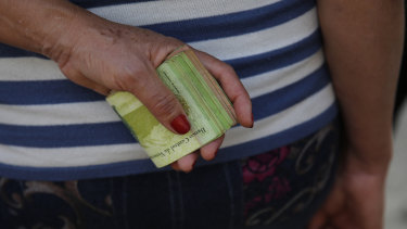 A woman holds a wad of bills to pay her bus fare in Caracas, Venezuela. 