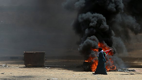 A Palestinian woman walks past burning tires near the Israeli border.
