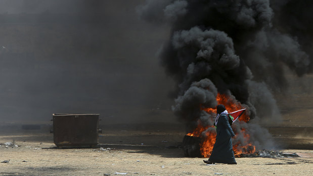 A Palestinian woman walks past burning tires near the Israeli border.