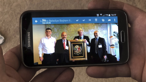 Mustafa Bal, former mayor of the village, second left, displays an image on his phone of his meeting with Boris Johnson holding an Ottoman Empire sign when he was Foreign Secretary, in Kalfat, Turkey.