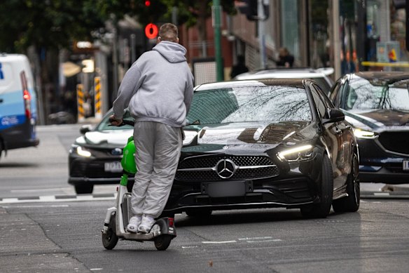 A man rides an e-scooter the wrong way down Little Bourke Street with no helmet in 2024, swerving to miss an oncoming car. 