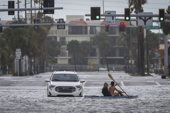 People kayak past an abandoned vehicle in St Pete Beach, Florida.