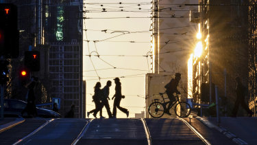 City workers crossing La Trobe St as the sun rises over the city of Melbourne on a warm winter day.