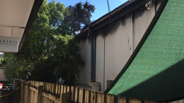 The wooden fence and partially-burned tree which separates the gutted complex (right) and Mr Bellas' cafe (left).