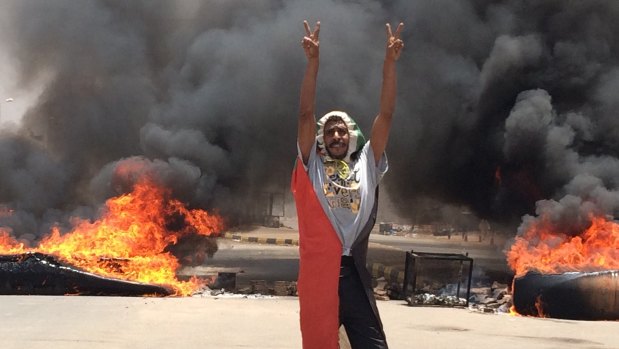 A protester flashes the victory sign in front of burning tires and debris on road 60, near Khartoum's army headquarters, in Khartoum, Sudan, before the military forces attacked,