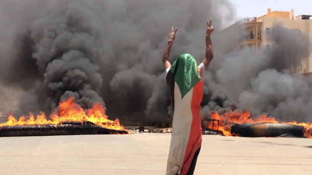 A protester wearing a Sudanese flag flashes the victory sign in front of burning tires and debris on road 60, near Khartoum's army headquarters, during the violence on Monday.